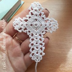 a hand holding a crocheted white object on top of a wooden table next to a book