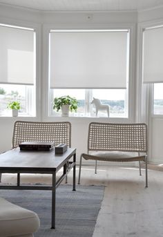 a living room with two chairs and a coffee table in front of three windows that have roman shades on them