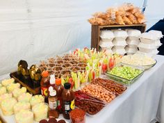 an assortment of food is displayed on a table with white linens and plastic cups