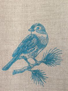 a small blue bird sitting on top of a piece of linen covered in beads and thread