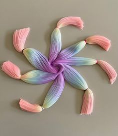 a flower made out of pink and blue yarn on a gray surface with the petals arranged in different colors