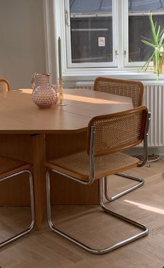 a wooden table with chairs around it in front of a window and potted plant