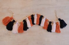 an orange, black and white tasselled necklace on a wooden surface with other tassels