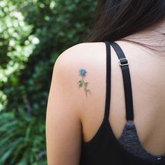 the back of a woman's shoulder with a small blue rose tattoo on it