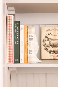 some books are sitting on top of a white book shelf with other books in it