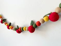 a garland made out of felt balls and leaves on a white wall with no one around it