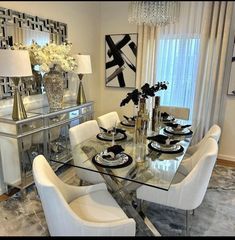 a glass dining table with white chairs and black plates on it in front of a window