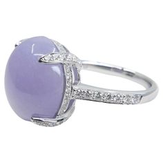 Please check out the HD Video! Here is a very eye pleasing lavender jade and diamond ring! It is certified natural jadeite jade. The ring is set in 18k white gold and diamonds. The center lavender jade cabochon is large at 11.36cts and measures 14.30mm x 12.90mm. There are a totaling of 0.45cts of white round brilliant natural diamonds that are in the prongs, shanks and hidden halo of the ring setting. The untreated / unenhanced natural jade is translucent. The jade color is the very desirable light lavender. We did not enclose or back the ring to improve the color since the lavender color is strong enough on its own. The jade is full of life. The ring is very pleasing to the eyes. A great three stone ring. Photos does not do this ring justice. This would be a great gift for that special s Luxury Lavender Round Ring, Luxury Jade Rings, Luxury Silver Jade Round Ring, Lavender Jade Ring, Oval Cabochon Jade Rings With Polished Finish, Lavender Ring, Ring Hidden Halo, Lavender Jade, Jade Color