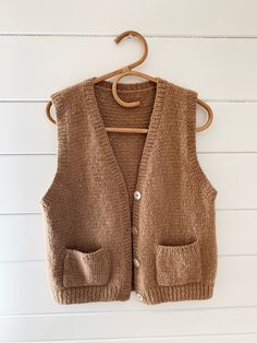 a brown sweater vest hanging on a white wall with a wooden hanger attached to it