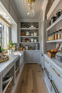 a kitchen with lots of white cabinets and shelves filled with pots, pans and bowls