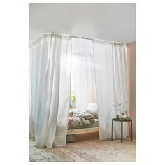 a bed sitting under a window next to a white curtain in a room with wooden floors