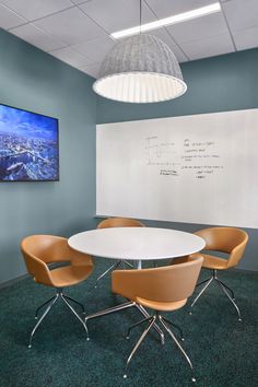 an office meeting room with chairs and a white board on the wall above it is a round table that has four orange chairs around it