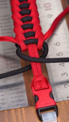 a close up of a red and black rope on a wooden table with measuring tape