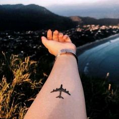 a person's arm with a small airplane tattoo on it, overlooking the ocean