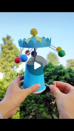 two hands holding up a blue cup with balls on it and a carousel in the background