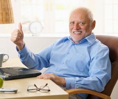 an older man sitting at a desk with his hand up in the air, giving a thumbs up