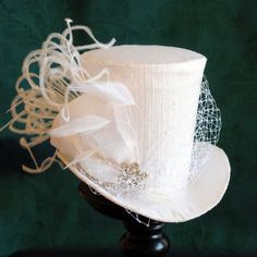 This simple and elegant bridal mini top hat is covered with beautiful white silk shantung. It is embellished with white veil, a luxurious spray of curled ostrich plums and a sparkling flower shaped rhinestone button. Also available in ivory and black here : https://www.etsy.com/shop/BizarreNoir?ref=seller-platform-mcnav&section_id=14329940 If you're interested in another color, please, send me a message to talk about your options. This mini top hat is fully lined with satin and attaches to t White Cap Mini Hat For Weddings, White Fitted Top Hat With High Crown, White High Crown Adjustable Mini Hat, White Adjustable High Crown Mini Hat, White Tall Crown Hat With Adjustable Fit, Fitted White Cloche Costume Hat, White Fitted Cloche Costume Hat, White Adjustable Tall Crown Hat, White Adjustable Hat With Tall Crown