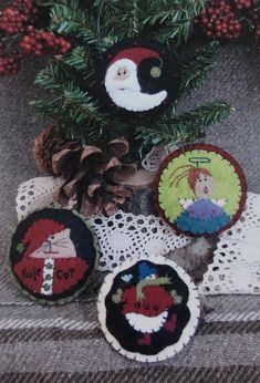 four christmas ornaments are sitting on a lace doily next to pine cones and berries