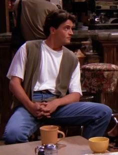 the young man is sitting in his living room with two coffee mugs on the table