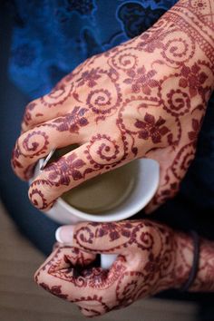 a person with henna on their hands holding a cup