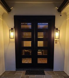 a black double door with two lights on each side and an entry mat in the middle