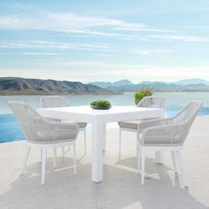 a white table with four chairs and a bowl of flowers on it near the water