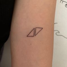 a small black triangle tattoo on the left inner arm, with two smaller triangles behind it