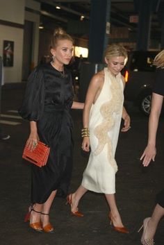 two women in black and white dresses are walking down the street with one woman carrying a red purse