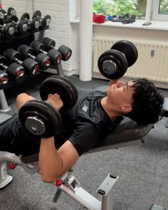 a man laying on top of a bench with two dumbbells in front of him