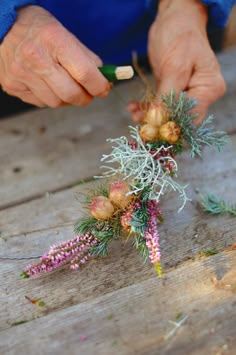 a person is arranging flowers on a wooden table with one hand and the other holding an object in their other hand