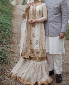 a man and woman standing next to each other on a dirt road in front of trees