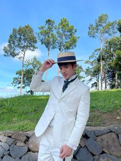 a man in a white suit and hat poses for the camera while holding his hat