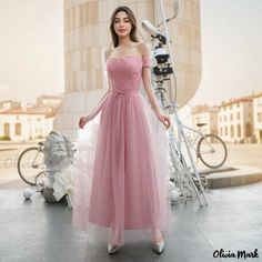 a woman standing in front of a building wearing a long pink dress with an off the shoulder neckline