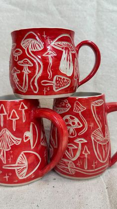 three red mugs with white designs on them