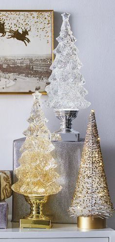 three glass christmas trees sitting on top of a white table next to a gold vase