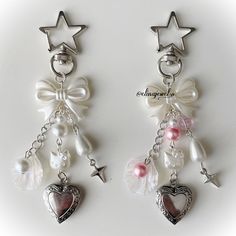 two pairs of earrings with charms attached to the earring hooks, one has a heart and star on it