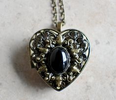 an ornate heart shaped locke with a black stone in the center on a silver chain