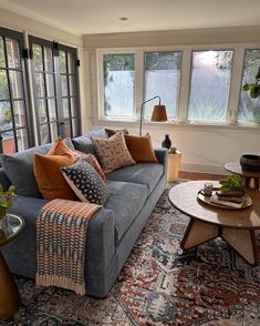 a living room filled with lots of furniture next to two large windows and a rug on the floor