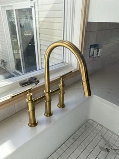 a gold faucet sitting next to a kitchen sink under a window in front of a house