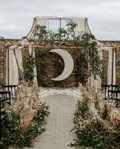 an outdoor wedding ceremony with greenery and a crescent moon on the wall behind it