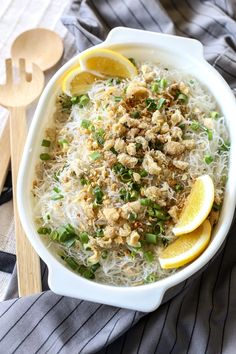 a white bowl filled with rice and lemons next to a wooden spoon on top of a striped cloth