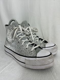 Elevate your style with these stunning Converse Chuck Taylor All Star Platform High sneakers. The unique design showcases glitter leopard spots on a silver background, making them a statement piece in any outfit. The high top shoe shaft style provides comfort and support, while the durable athletic material ensures long-lasting wear. These sneakers feature a US shoe size of 8 and a style code of 572043C. The Converse brand is renowned for its quality and style, making these shoes a must-have for Silver High-top Sneakers With Perforations, Trendy Metallic High-top Sneakers, Silver Lace-up High-top Sneakers For Streetwear, Silver Sneakers For Streetwear With Speckled Midsole, Silver Sneakers With Speckled Midsole For Streetwear, Metallic Sneakers With Speckled Midsole For Streetwear, Casual Silver High-top Lace-up Sneakers, Metallic High-top Sneakers With Speckled Midsole, Casual Silver Glitter Sneakers