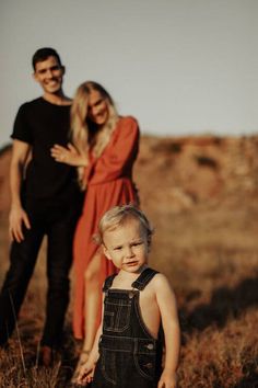 a man and woman standing next to a little boy in a field with tall grass