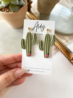 a person holding up a pair of cactus earrings