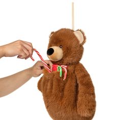 a person holding a teddy bear with a candy cane in it's mouth and another hand