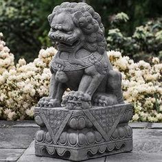 a statue of a lion sitting on top of a stone block in front of flowers