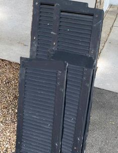 two black shutters on the side of a building next to a sidewalk and door