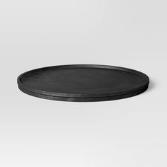 an empty black plate sitting on top of a white surface with no one around it