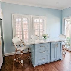 a kitchen with blue walls and wooden floors has an island in the middle that is surrounded by chairs