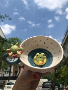 a hand holding up a small bowl with two little frog figurines in it